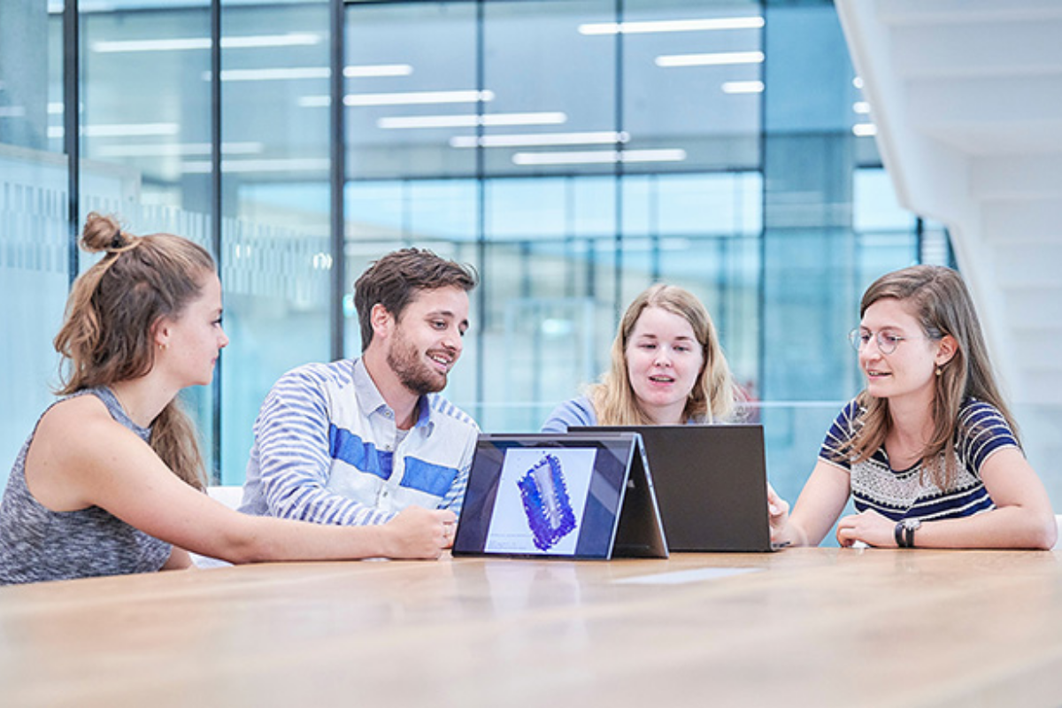Four students sitting at a table and discussing of a tablet computer